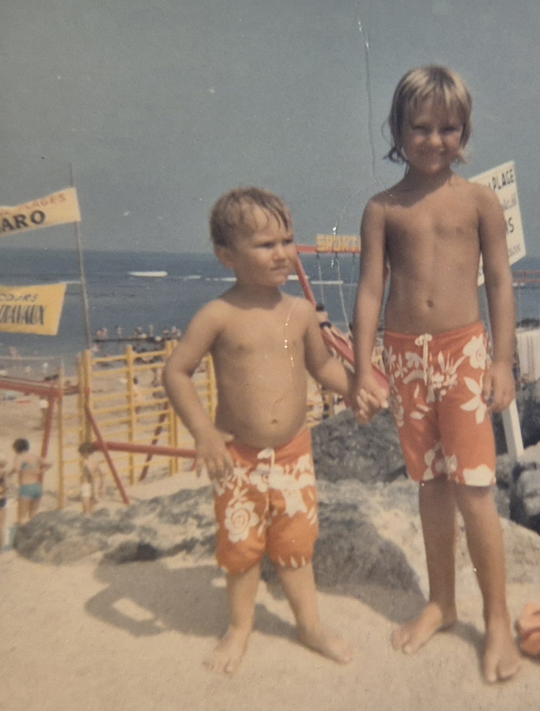 Deux enfants en maillots oranges se tenant la main face à l'océan, côte basque