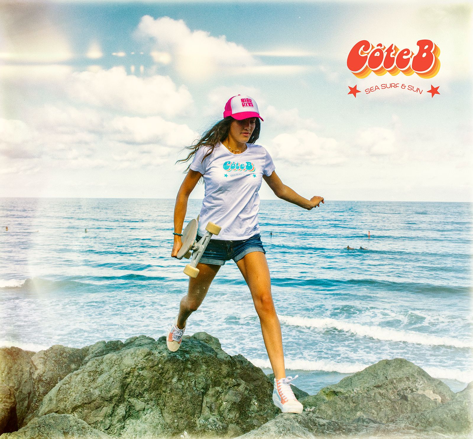 Fille en tee-shirt blanc Côte B et casquette rose sur les rochers face à l'océan — @coteb_biarritz